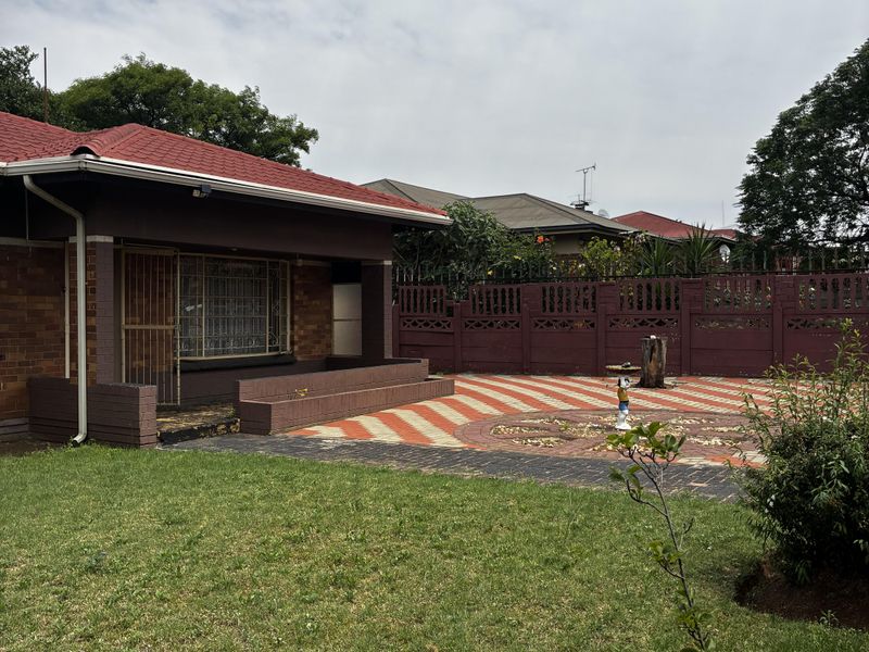 Rear view of the house featuring a paved patio area, brick facade, tiled roof, and a well-maintained garden with boundary walling.