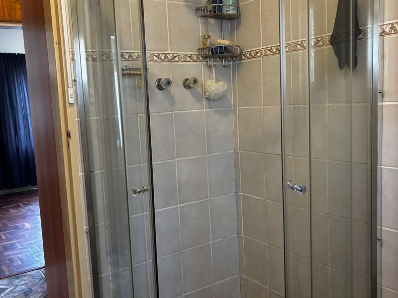 A functional bathroom featuring a curved glass shower enclosure with tiled walls and flooring, showing signs of age in the grout.