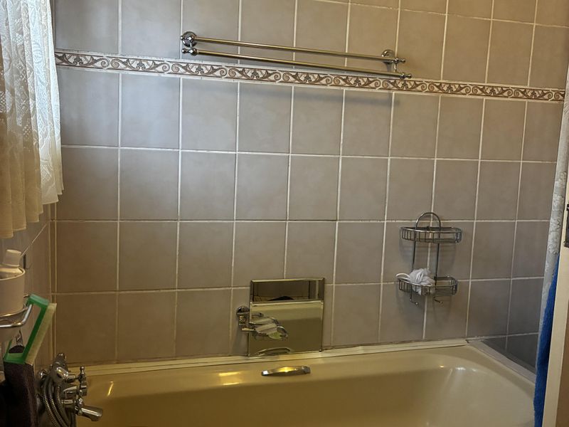 A functional bathroom featuring a bathtub, pedestal basin, and tiled walls. The space is dated and would benefit from modern updates to finishes.