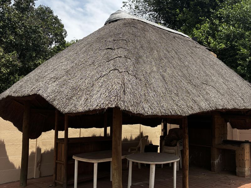 Outdoor thatched lapa area featuring a built-in braai and brick paved flooring, providing a rustic space for outdoor entertainment.