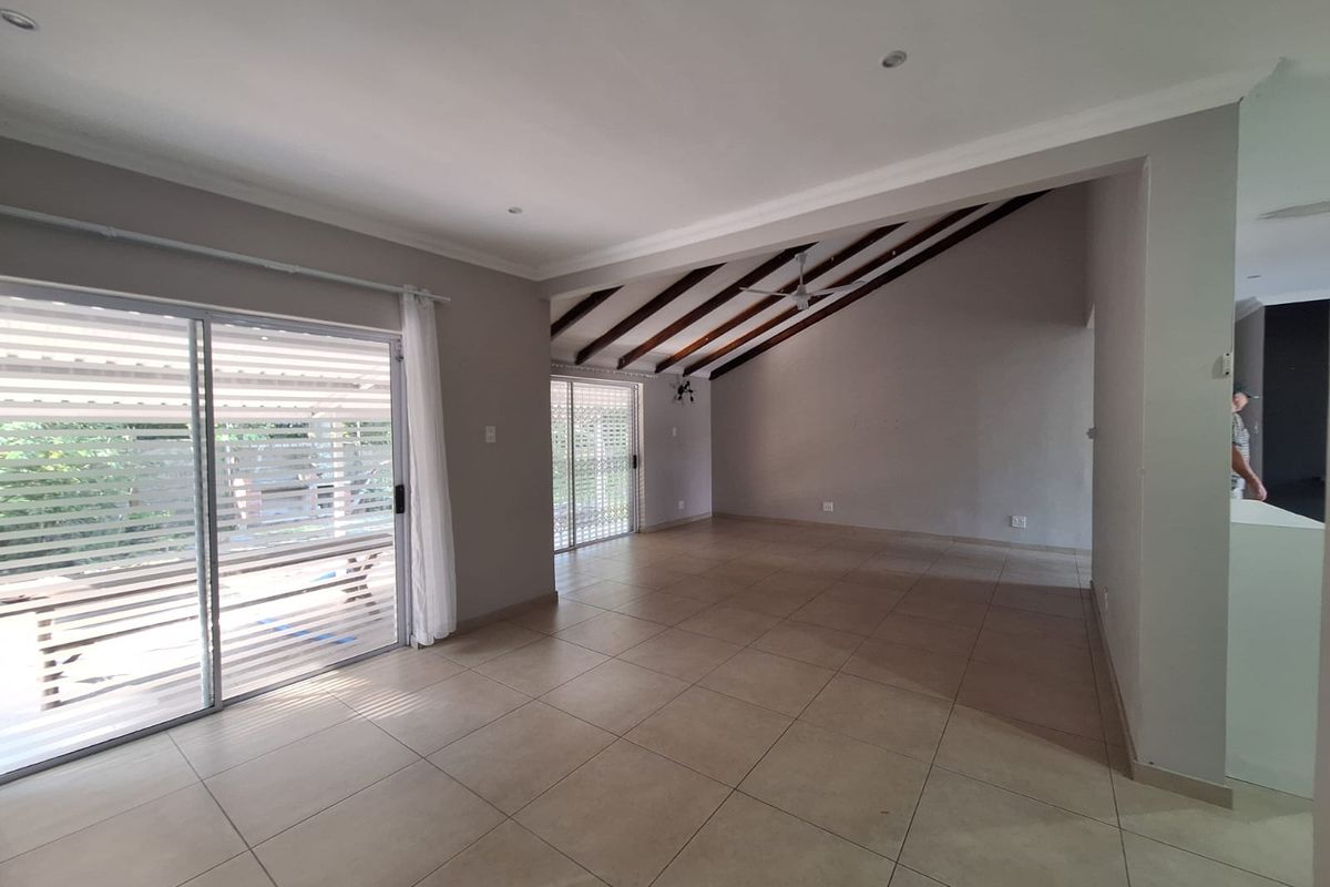 Spacious, light-filled living area featuring large format floor tiles, exposed timber ceiling beams, and sliding glass doors providing access to the outdoor patio.