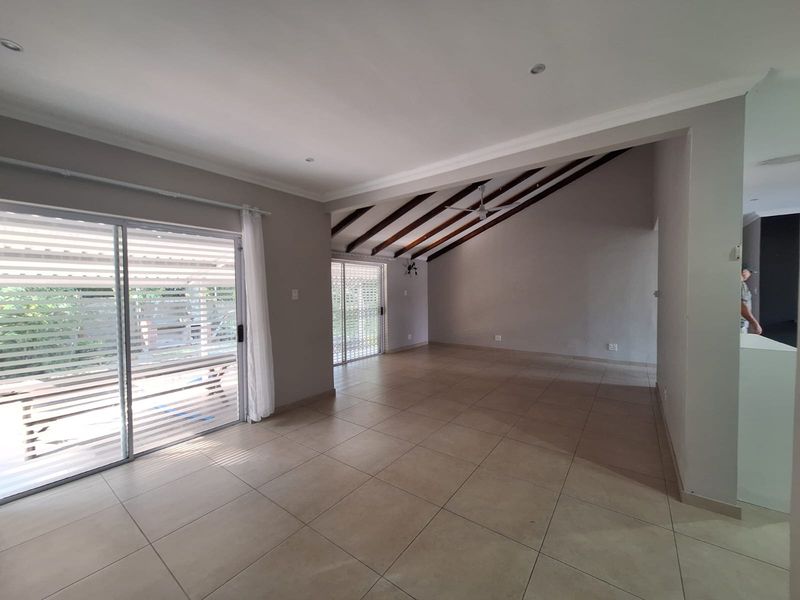 Spacious, light-filled living area featuring large format floor tiles, exposed timber ceiling beams, and sliding glass doors providing access to the outdoor patio.