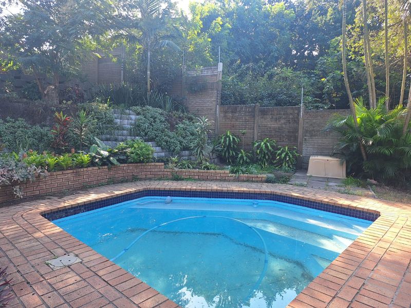 A private swimming pool area featuring brick coping, a tiered brick retaining wall, and established garden landscaping.