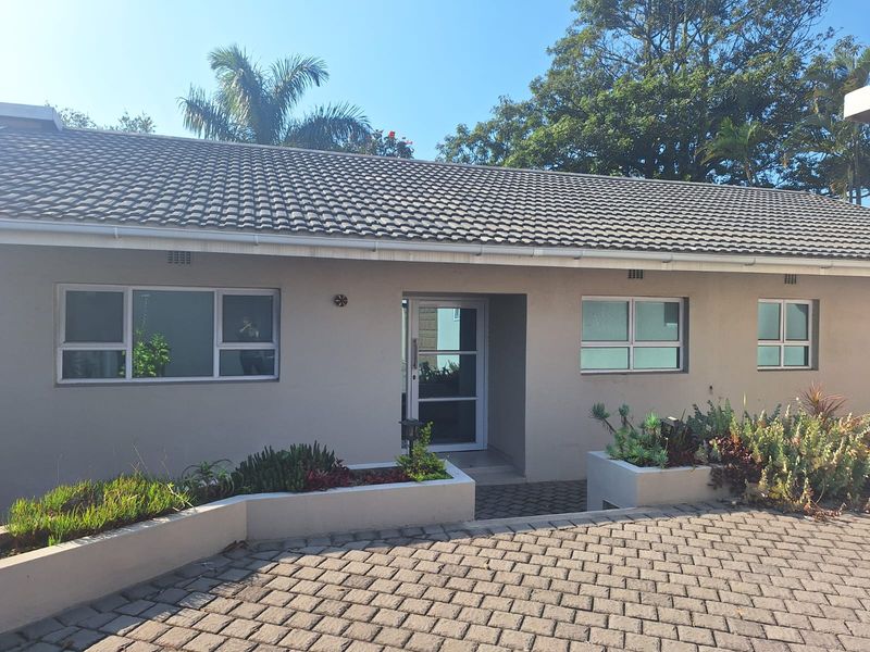 Front elevation of a single-story house featuring a tiled roof, aluminium window frames, and a paved driveway with integrated concrete garden planters.