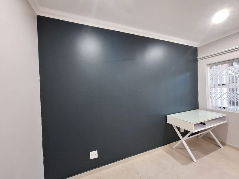 A well-maintained bedroom featuring a dark accent wall, tiled flooring, recessed lighting, and a window fitted with a security gate.