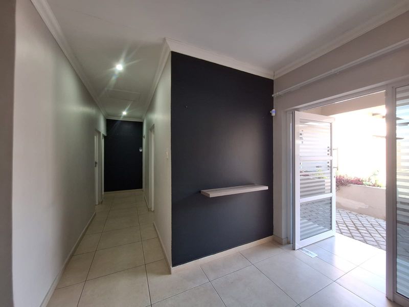 A bright, modern hallway featuring neutral tiled flooring, recessed lighting, and a striking dark accent wall with a built-in floating shelf.
