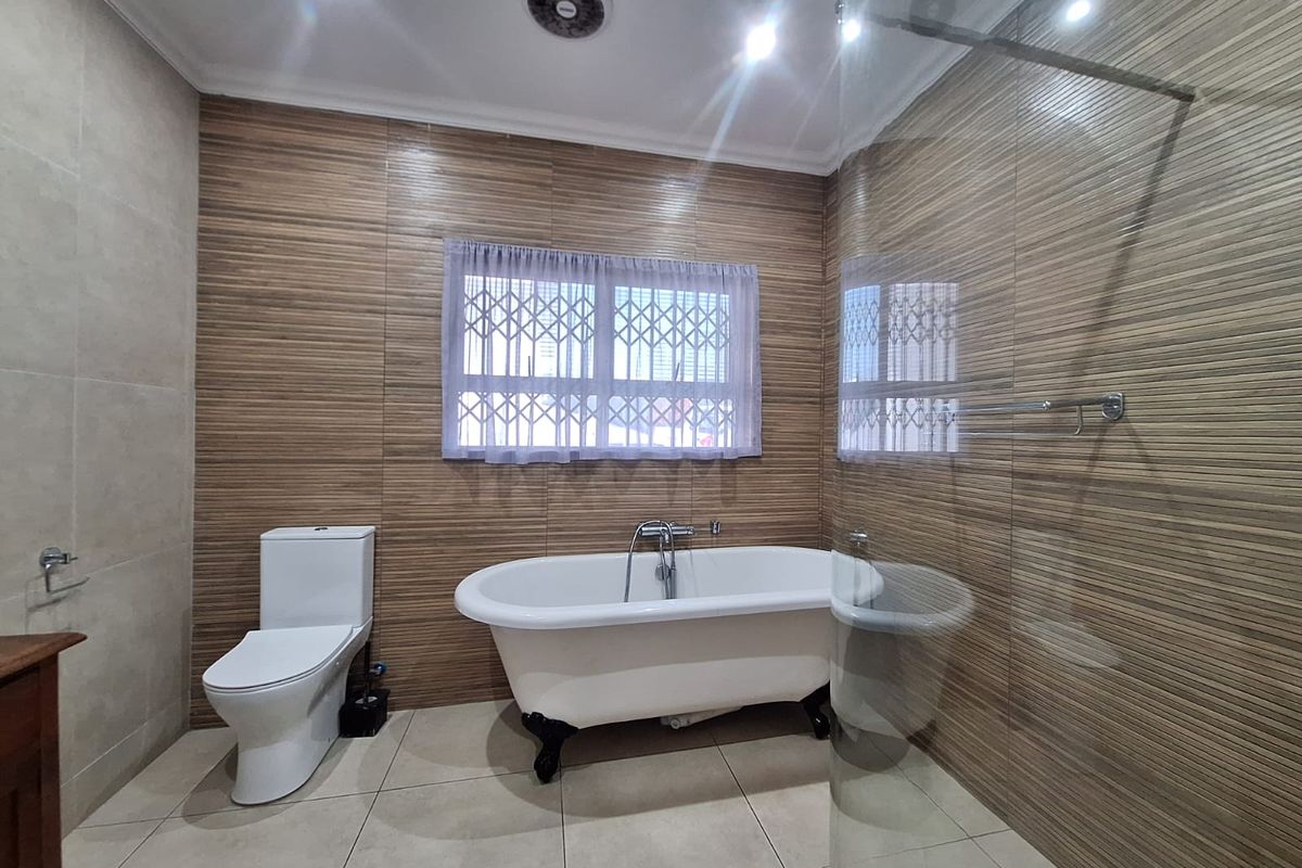 A modern bathroom featuring a freestanding bathtub, a glass-enclosed shower, and contemporary tiled finishes with a secure window.