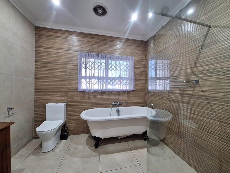 A modern bathroom featuring a freestanding bathtub, a glass-enclosed shower, and contemporary tiled finishes with a secure window.