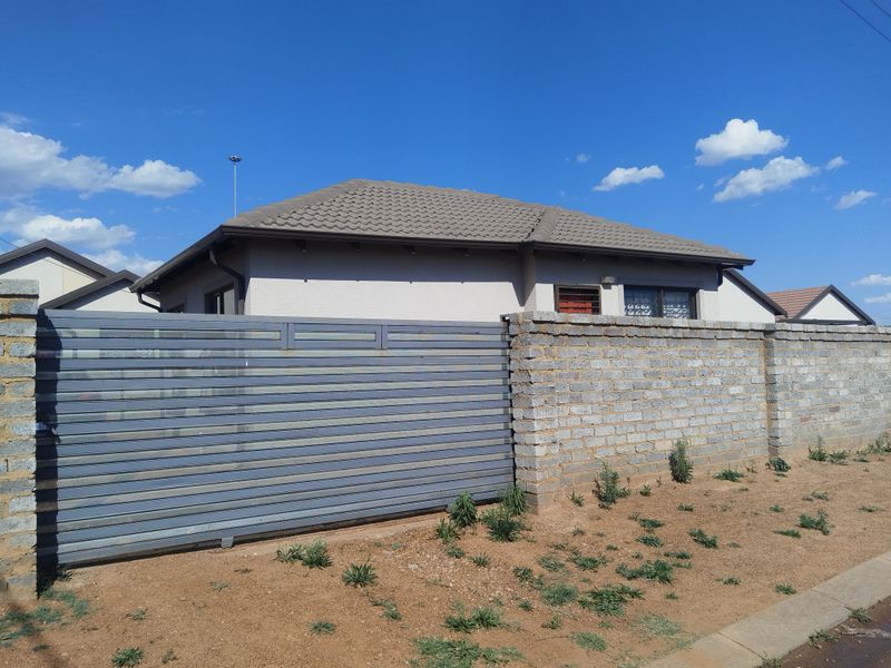 Front view of a residential property featuring a concrete tile roof, brick boundary wall, and a secure sliding metal gate.