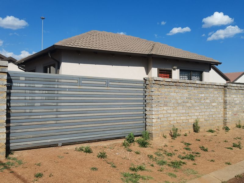 Exterior view of a residential property featuring a sliding metal gate, face brick boundary wall, and concrete tiled roof.