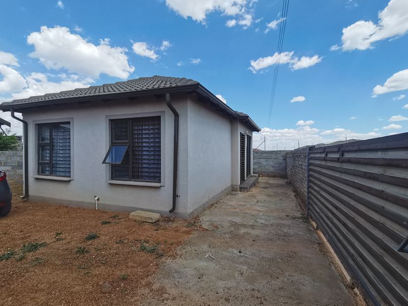 Rear view of the property featuring a tiled roof, aluminium window frames, and a concrete apron area enclosed by a boundary wall and metal fencing.