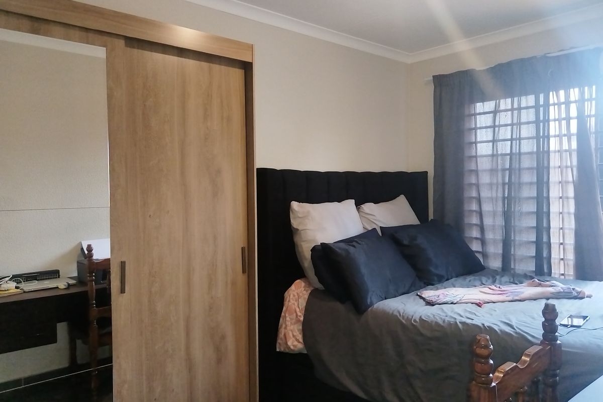 A comfortable bedroom featuring a modern built-in wardrobe with sliding mirror doors and neutral wall finishes.