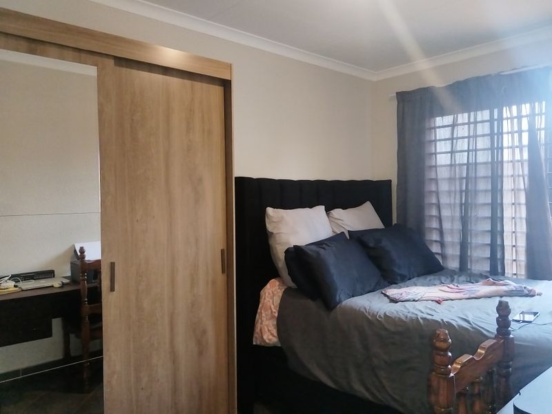A comfortable bedroom featuring a modern built-in wardrobe with sliding mirror doors and neutral wall finishes.
