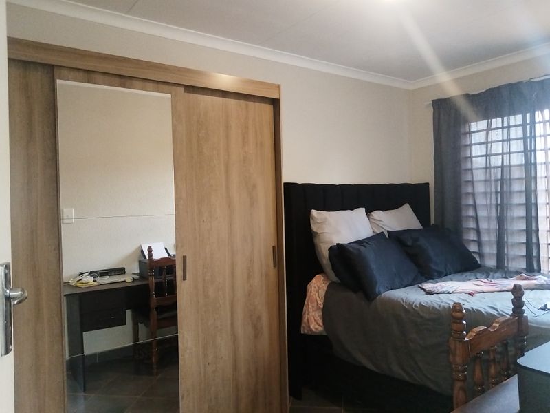 A well-maintained bedroom featuring a modern wood-finish built-in wardrobe with a mirrored panel, tiled flooring, and neutral wall tones.