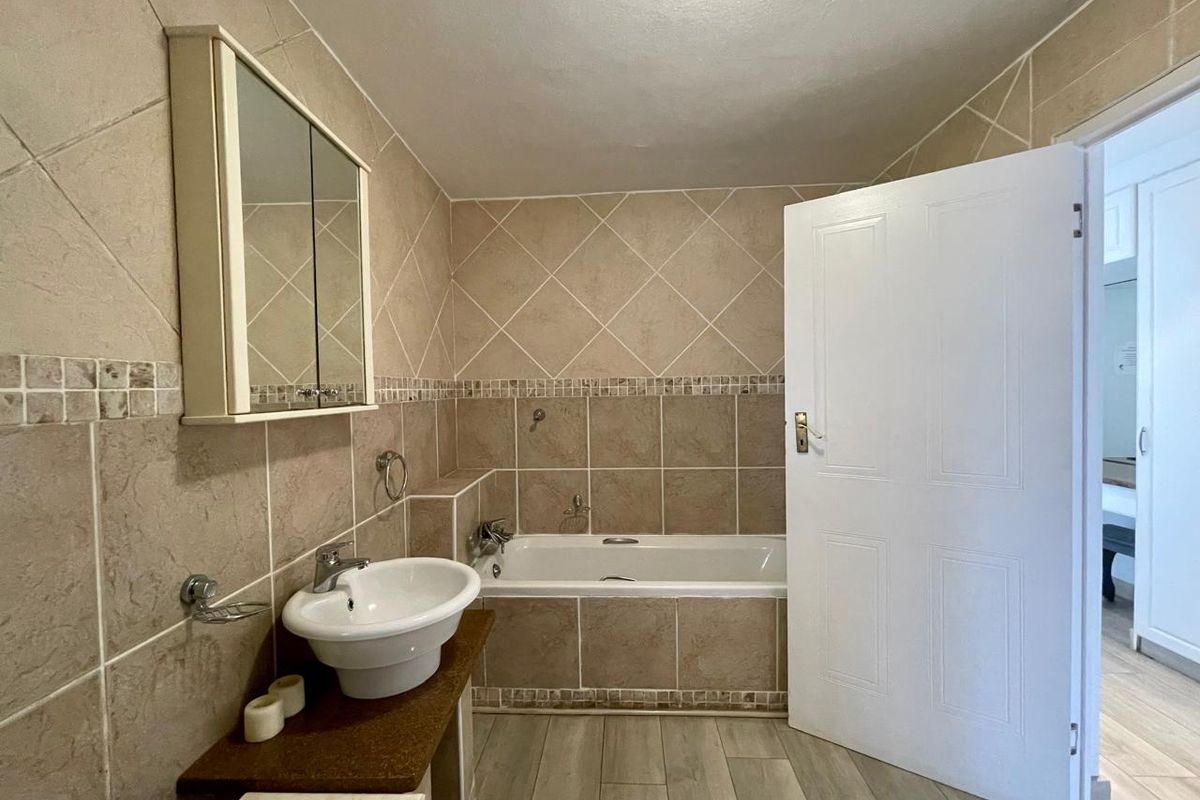 A functional bathroom featuring a built-in bathtub, wall-mounted basin, and mirrored medicine cabinet, finished with neutral ceramic wall tiles and tiled flooring.
