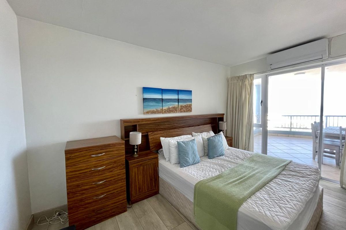 A well-maintained bedroom featuring tiled flooring, a wall-mounted air conditioning unit, and direct access to a private balcony through sliding glass doors.
