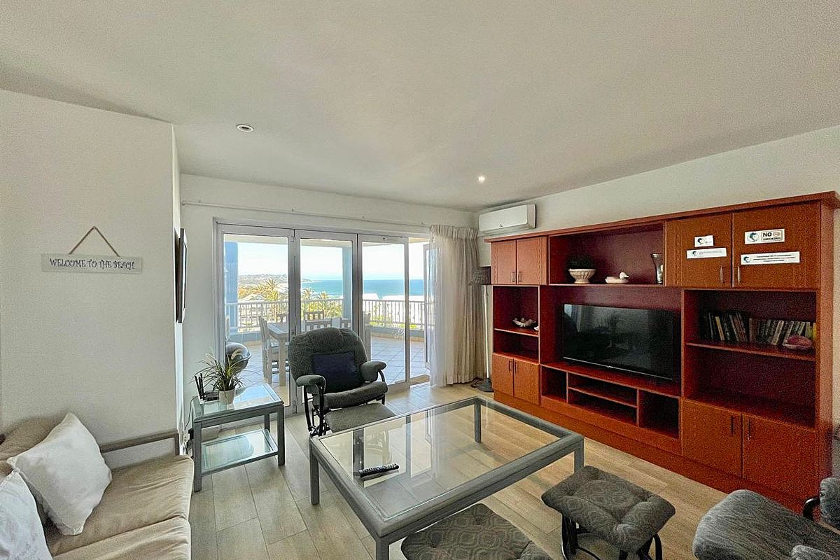 A living room featuring a large built-in wooden wall unit, tiled flooring, and sliding glass doors that open onto a balcony with ocean views.