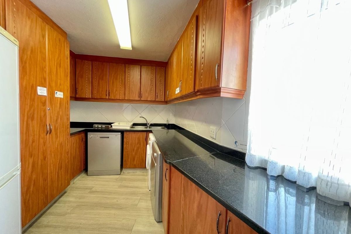 A functional kitchen featuring wood-look cabinetry, dark granite countertops, tiled backsplash, and integrated appliance spaces with modern laminate flooring.