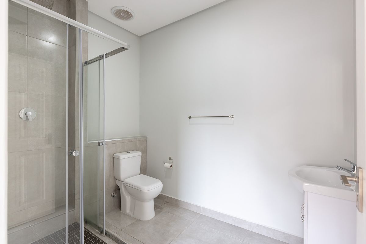 A clean, modern bathroom featuring a glass-enclosed shower, white ceramic toilet, and a vanity basin with chrome fixtures.