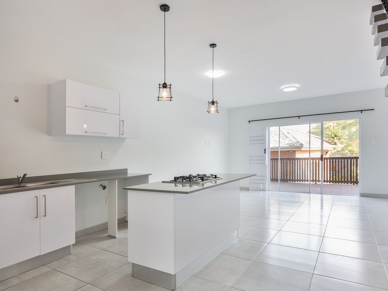 Modern open-plan kitchen and living area featuring a central island with gas hob, sleek white cabinetry, tiled floors, and access to a balcony.