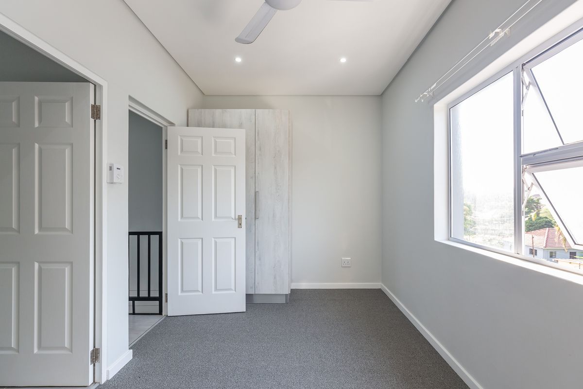 A clean, neutral bedroom featuring built-in cabinetry, carpeted flooring, and a ceiling fan, offering a bright and versatile space.