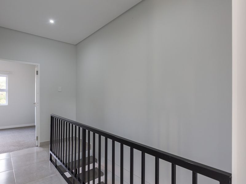 A bright and modern hallway featuring tiled flooring, a sleek black metal balustrade, and recessed downlighting, leading to an adjacent bedroom.