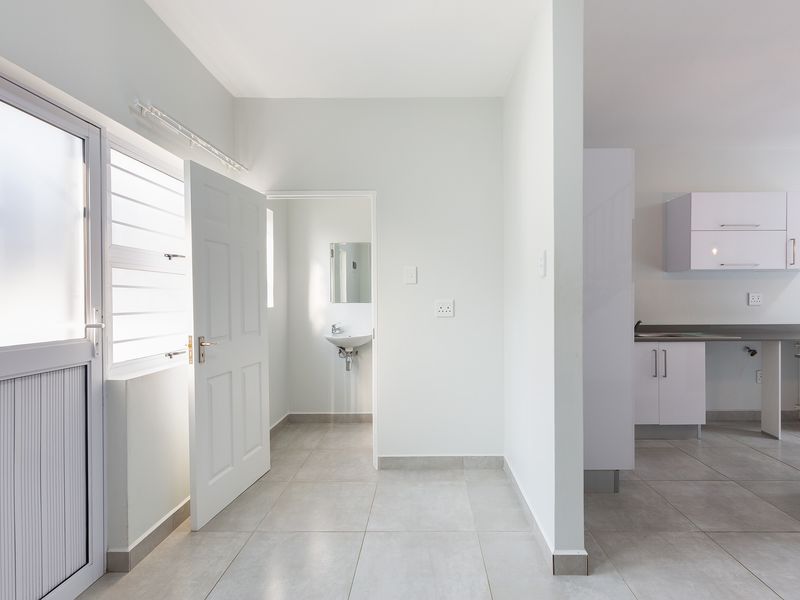 An open-plan living area featuring neutral tiled flooring, a modern kitchen with white cabinetry, and an adjacent bathroom with a basin.
