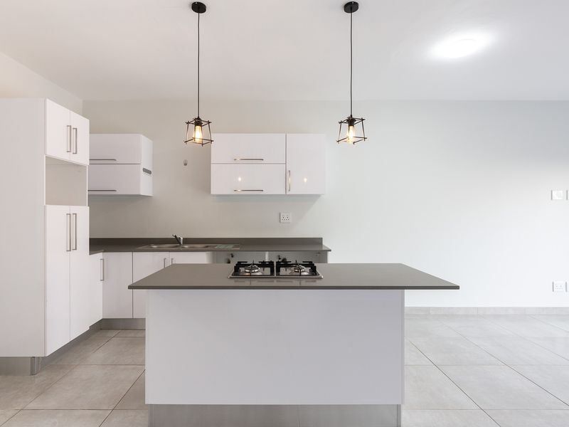 Modern, minimalist kitchen featuring white cabinetry, a central island with a built-in gas hob, and sleek tiled flooring in an open-plan layout.
