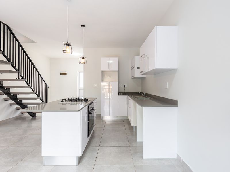 Modern open-plan kitchen featuring a central island with a gas hob, sleek white cabinetry, and an adjacent staircase with a contemporary metal railing.