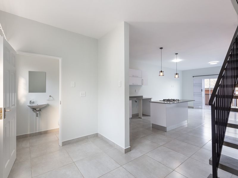 Spacious open-plan living area featuring a modern kitchen with island, gas hob, tiled flooring, and an adjacent guest bathroom with a staircase.