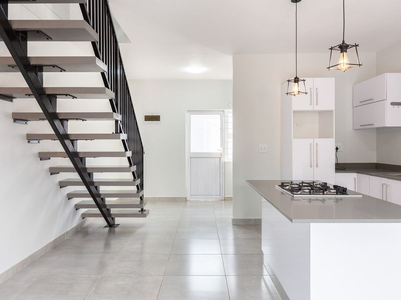 Modern open-plan living area featuring a sleek kitchen with stone countertops, gas hob, and a striking contemporary staircase with metal balustrade.