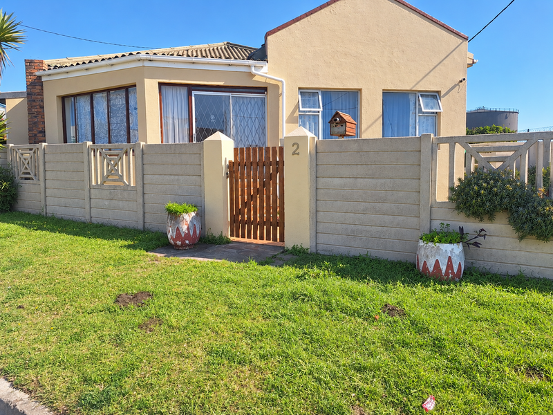 Front elevation of a single-story house featuring a precast concrete boundary wall, timber pedestrian gate, and tiled roof with aluminium window frames.