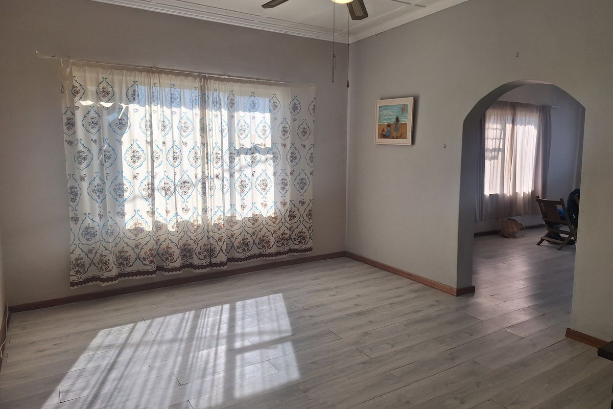 A bright, empty living room featuring light-toned laminate flooring, a ceiling fan, and a classic arched doorway leading to an adjacent space.