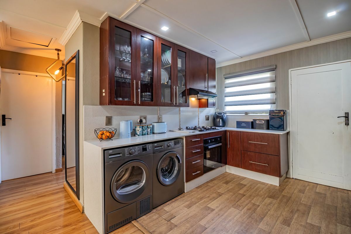 A well-maintained kitchen featuring dark wood cabinetry, stone countertops, integrated gas hob, under-counter oven, and laminate flooring with space for laundry appliances.
