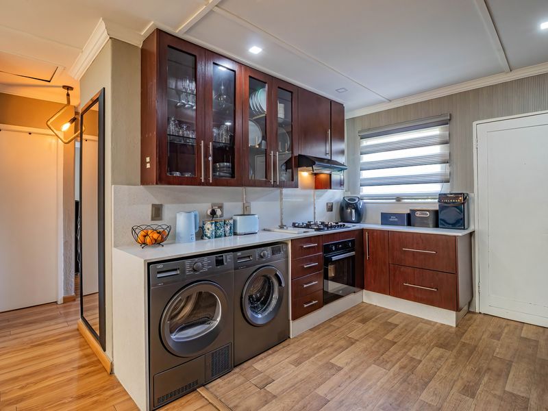 A well-maintained kitchen featuring dark wood cabinetry, stone countertops, integrated gas hob, under-counter oven, and laminate flooring with space for laundry appliances.