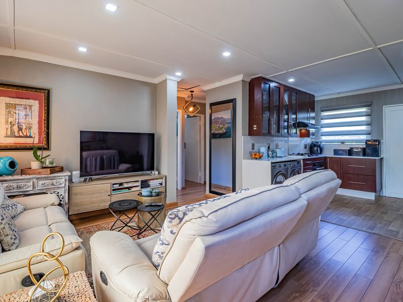 An open-plan living area featuring laminate flooring, recessed lighting, and a compact kitchen with built-in cabinetry and integrated appliances.