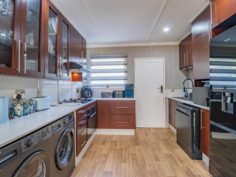 A well-maintained kitchen featuring dark wood cabinetry, stone countertops, integrated appliances, and durable laminate flooring with a functional layout.