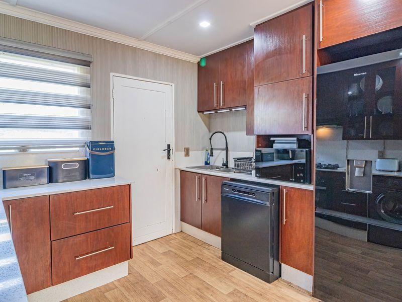 A functional kitchen featuring dark wood cabinetry, laminate countertops, integrated appliances, and a modern gooseneck faucet, providing efficient workspace and storage.