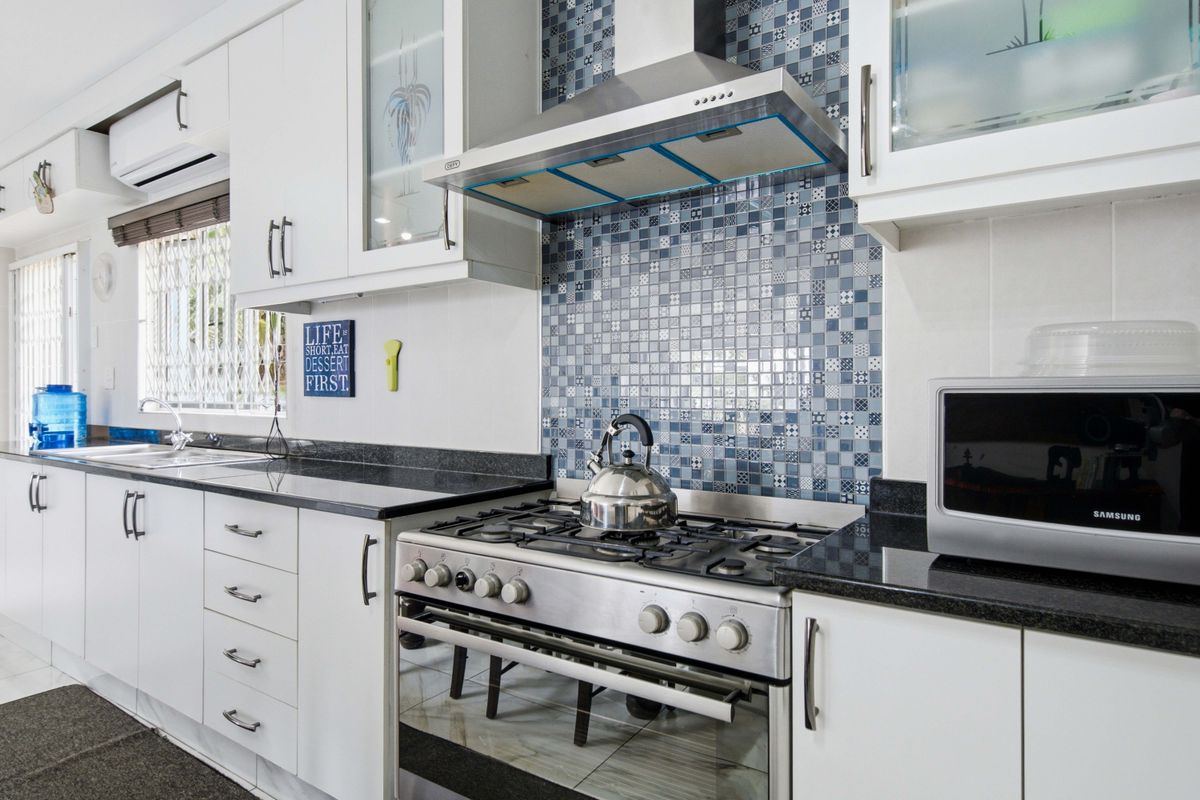 A well-maintained kitchen featuring white cabinetry, granite countertops, a mosaic tile backsplash, and a stainless steel gas stove with an integrated extractor fan.