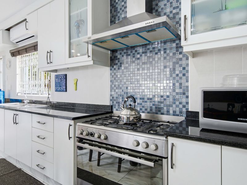 A well-maintained kitchen featuring white cabinetry, granite countertops, a mosaic tile backsplash, and a stainless steel gas stove with an integrated extractor fan.