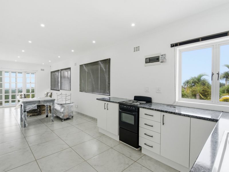 Bright open-plan kitchen and living area featuring modern white cabinetry, granite countertops, tiled floors, and large windows providing ample natural light.