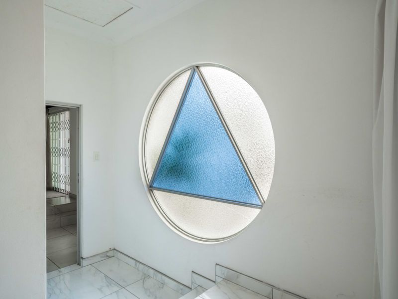A bright hallway featuring a unique circular window with a triangular blue glass insert and clean tiled flooring.