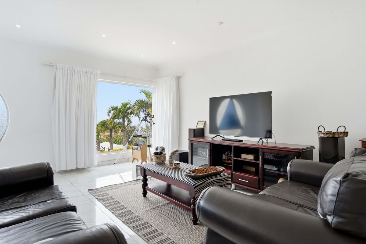 A bright and spacious living room featuring large windows with garden views, recessed lighting, and polished tiled flooring.