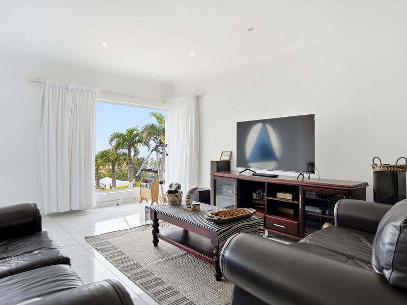 A bright and spacious living room featuring large windows with garden views, recessed lighting, and polished tiled flooring.