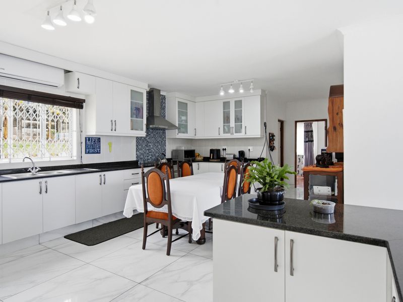 Spacious open-plan kitchen and dining area featuring white cabinetry, granite countertops, tiled flooring, and a wall-mounted air conditioning unit.