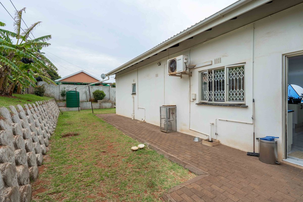 Rear exterior view featuring a paved walkway, retaining wall, and air conditioning unit along the side of the house.