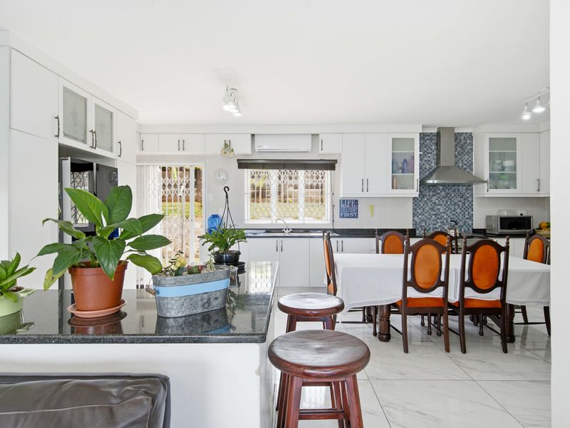 Spacious open-plan kitchen and dining area featuring modern white cabinetry, granite countertops, a mosaic backsplash, and sleek tiled flooring with direct outdoor access.