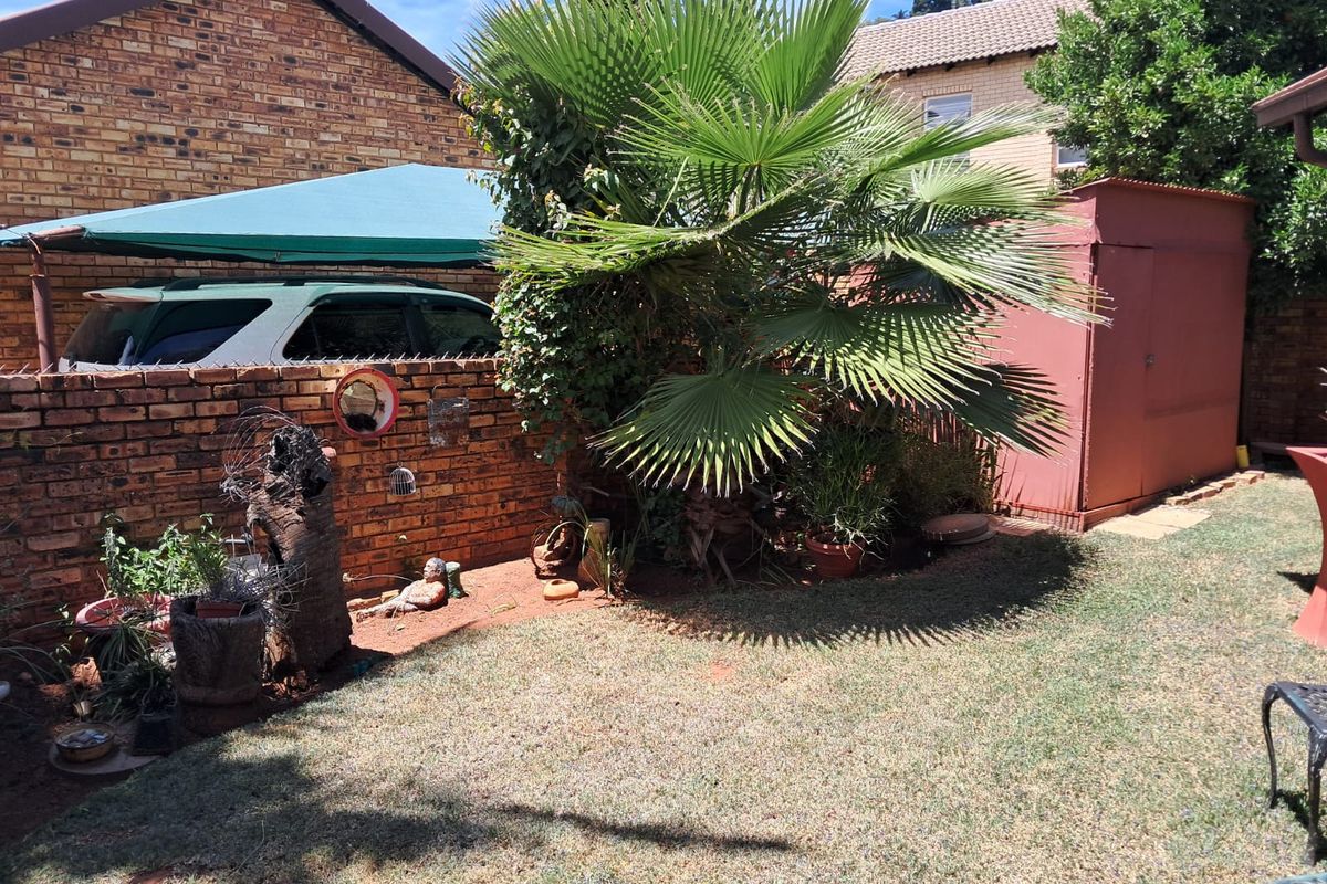 A rear garden area featuring a lawn, a brick boundary wall, a metal storage shed, and a shade sail structure.