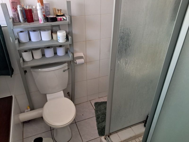 A functional bathroom featuring a standard toilet, tiled walls and flooring, and a glass-enclosed shower area.