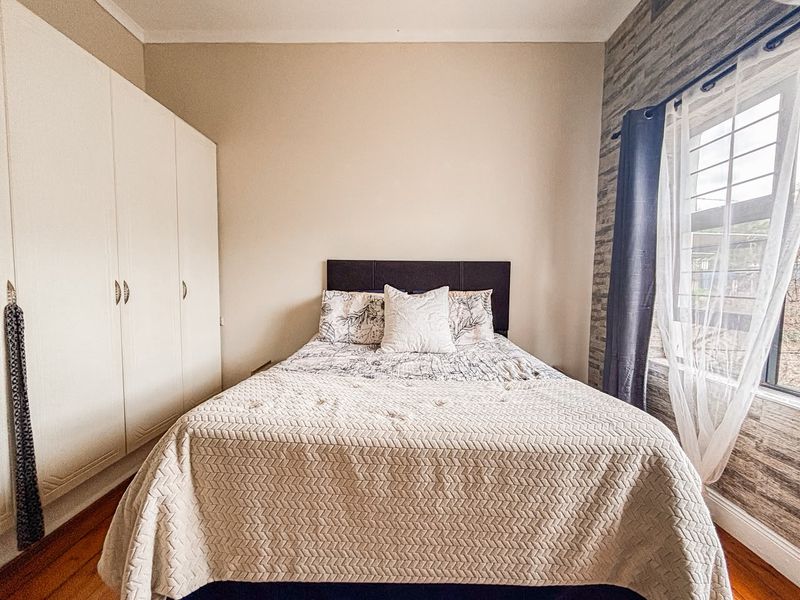 A well-maintained bedroom featuring built-in cupboards, warm wooden flooring, and a decorative feature wall with natural light.